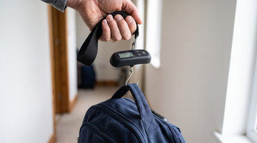 Compact 50 kg digital hanging scale held by its strap weighing a suspended travel bag